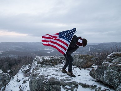 Man holding an American flag in snowy mountains.
