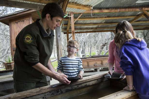 Stuart Kelly, a season park aide, helps six-year-old Ryan Sherman, Jennifer Sherman and and nine-year-old Emma Sherman (left to right) pan for gold at the Marshall Gold Discovery State Historic Park in Coloma, Calif., on Saturday, March 4, 2017. The park encompasses most of the historic town of Coloma where gold was found by James Marshall in 1848.