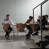 A man in a work setting looks disgusted as he glances at a group of coworkers sitting a table away