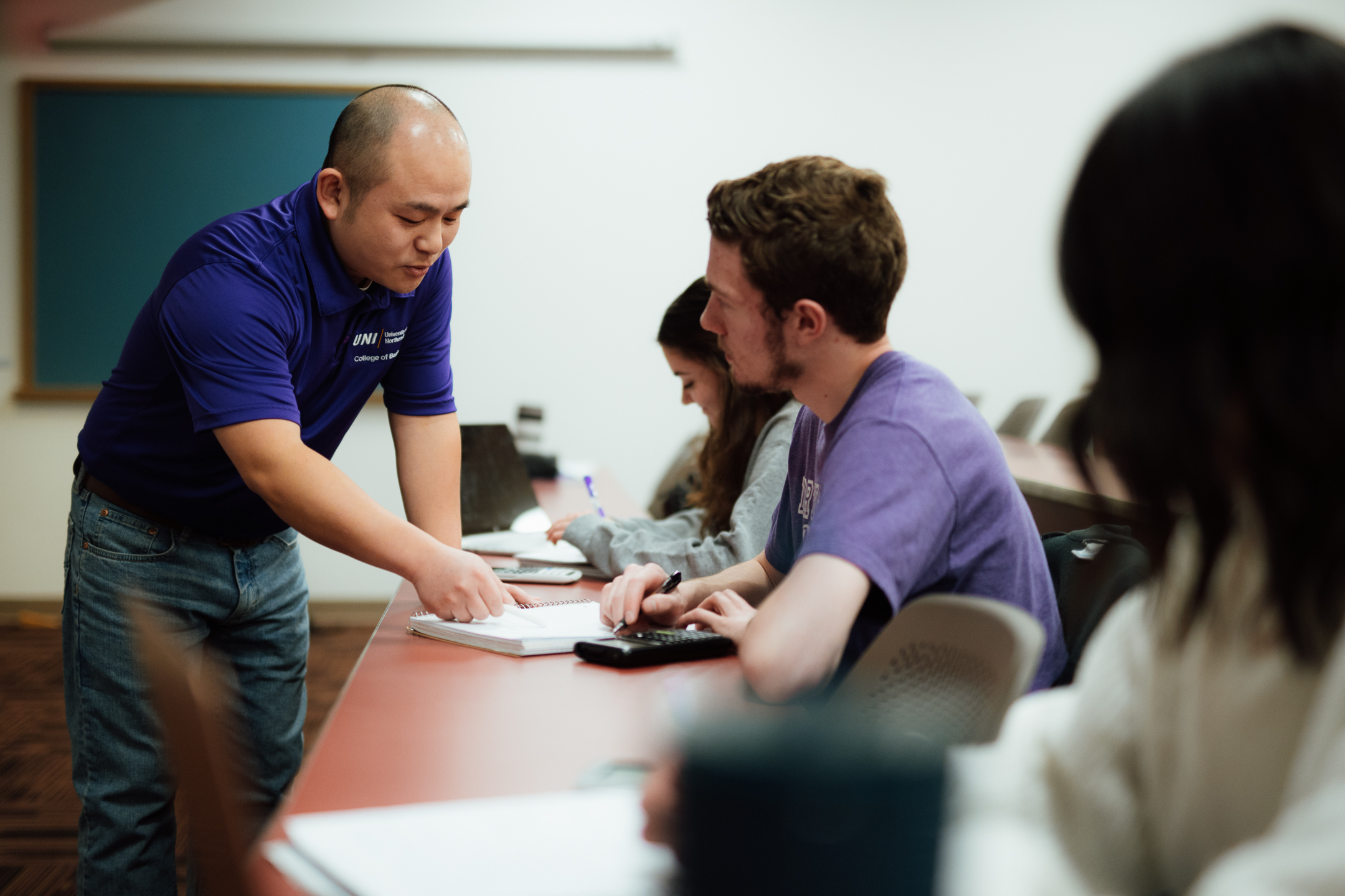 Image showing a professor leading a class and assisting an individual student with the notes.