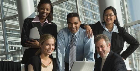 Group of five smiling executives posing in front of office window