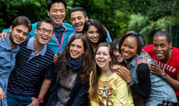10 international students smiling and gathered closely together for a group photo in a green area.