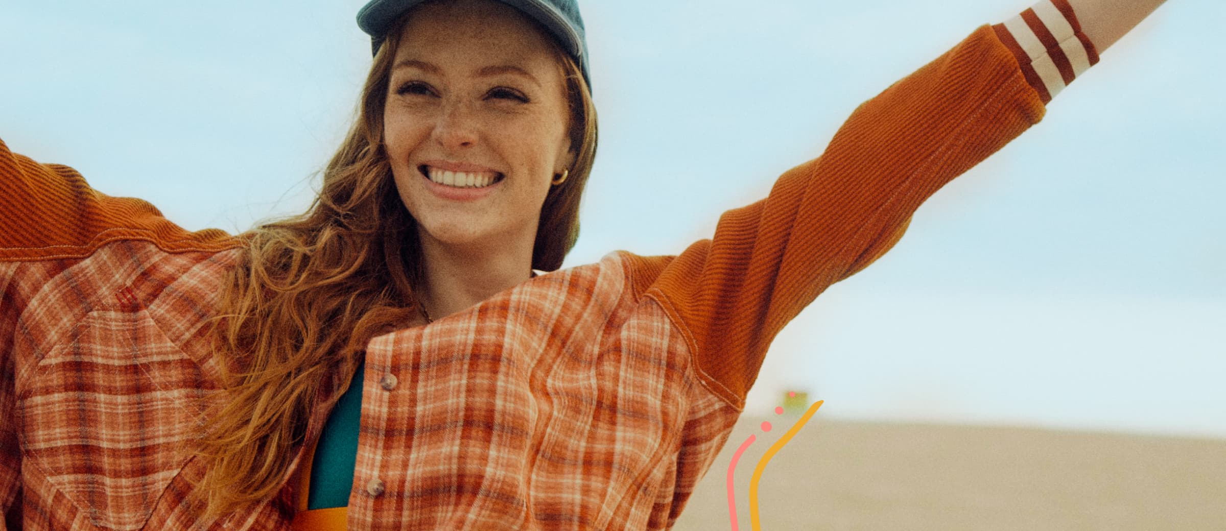 Smiling woman in an orange sweater and cap taking a selfie at the beach