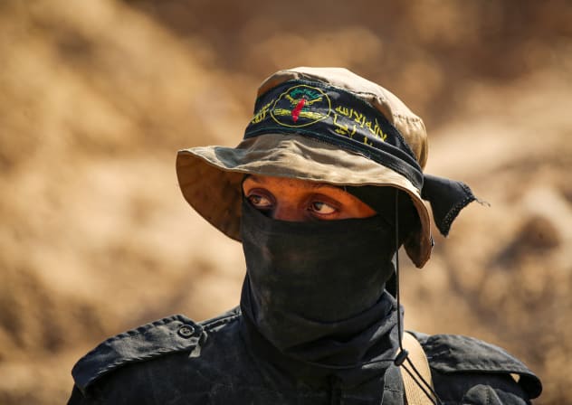 A masked gunman from the Palestinian Islamic Jihad movement keeps watch as others search for bodies in Nuseirat in the central Gaza Strip on November 21, 2025.