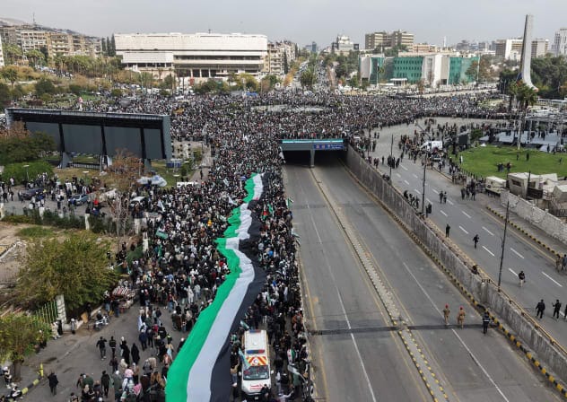 A drone view shows people carrying a giant, long flag on the day of a military parade, as Syrians mark the first anniversary of Bashar al-Assad's fall, in Damascus, Syria December 8, 2025. 