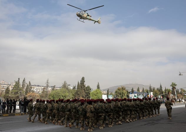A helicopter flies above military personnel performing during a military parade, as Syrians mark the first anniversary of Bashar al-Assad's fall, in Damascus, Syria, December 8, 2025.