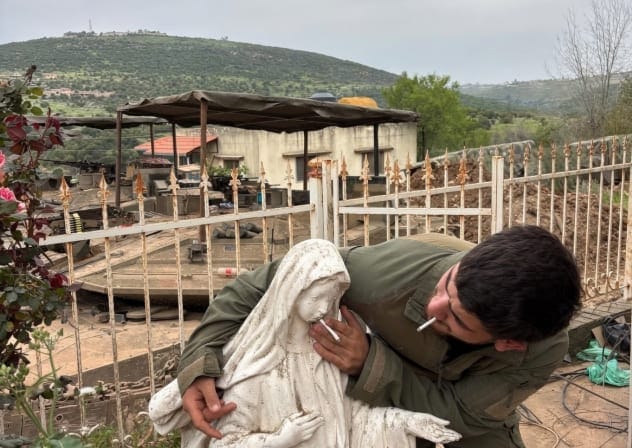 AN IDF soldier puts a cigarette in the mouth of a statue of the Virgin Mary.