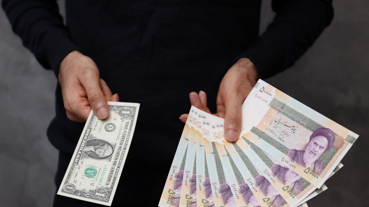 A currency dealer poses for a photo with a U.S one dollar bill and the amount being given when converting it into Iranian rials in an exchange shop in Tehran, Iran December 25, 2022