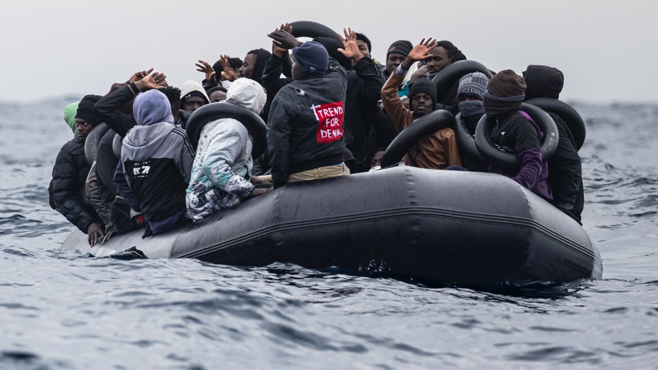 Migrants onboard a rubber boat wave and gesture as they wait to be rescued by crew members of the "Ocean Viking" rescue ship in the search-and-rescue zone off the international waters of Libya, on January 16, 2026.
