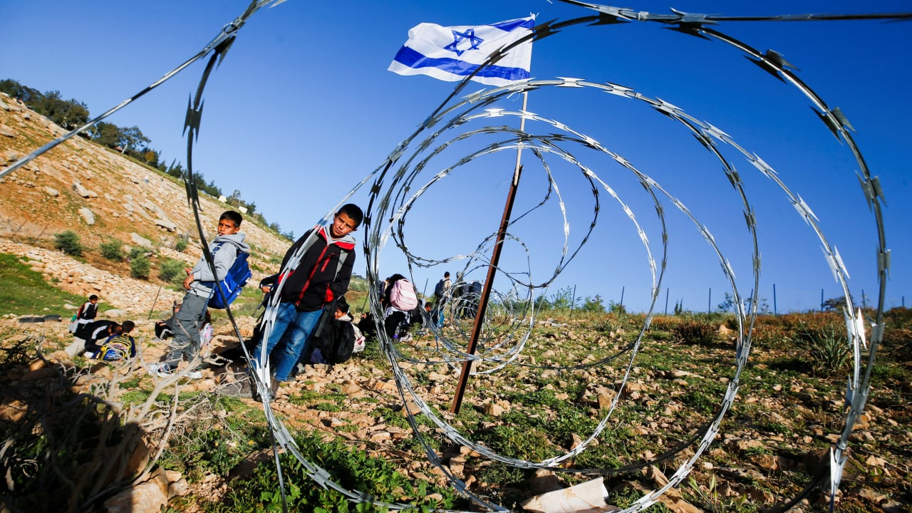 PALESTINIAN STUDENTS gather near a fence installed by Israeli settlers on their way to school, near Umm al-Khair in the West Bank, on April 14, 2026.