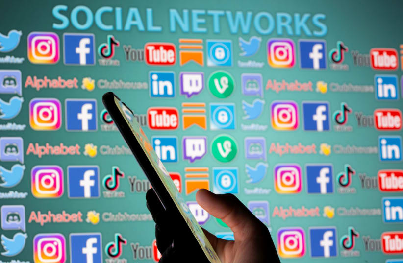 Woman with smartphone is seen in front of displayed social media logos in this illustration taken, May 25, 2021. (photo credit: REUTERS/DADO RUVIC/ILLUSTRATION)