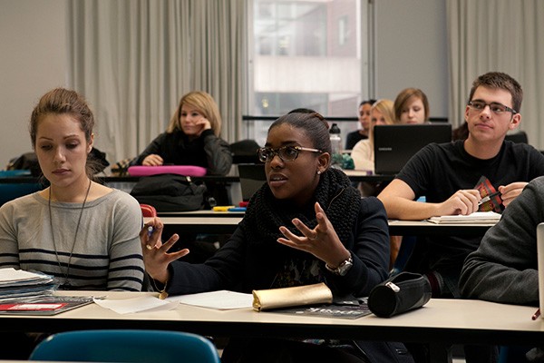 Students in a lecture hall with one student speaking and gesturing.