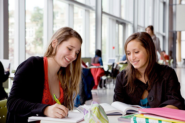 Two students smiling working at a table with books in front of them