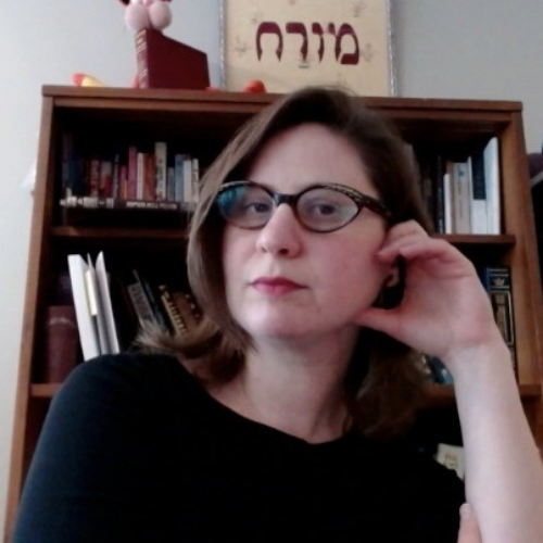 Annie, wearing a black sweater, is in front of a brown bookshelf.