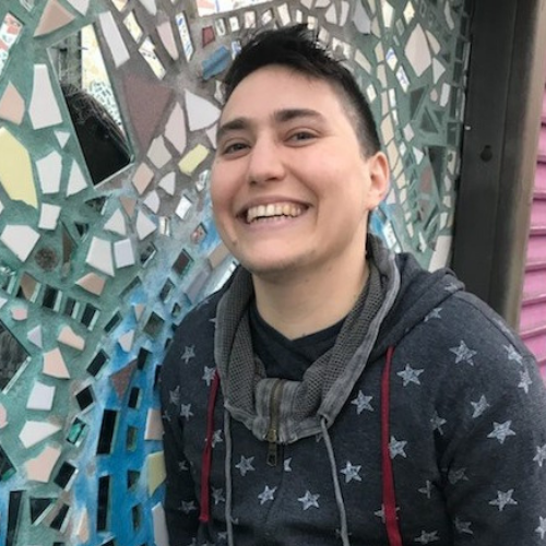 Noah stands in front of a mosaic background. He is wearing a navy hoodie with stars on it.